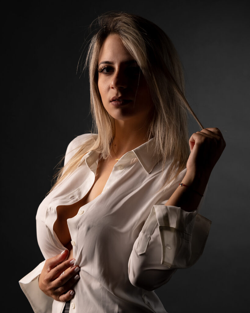 Blonde woman wearing an open white button-down shirt posing confidently against a dark background, photographed at Duette Studio in Miami.